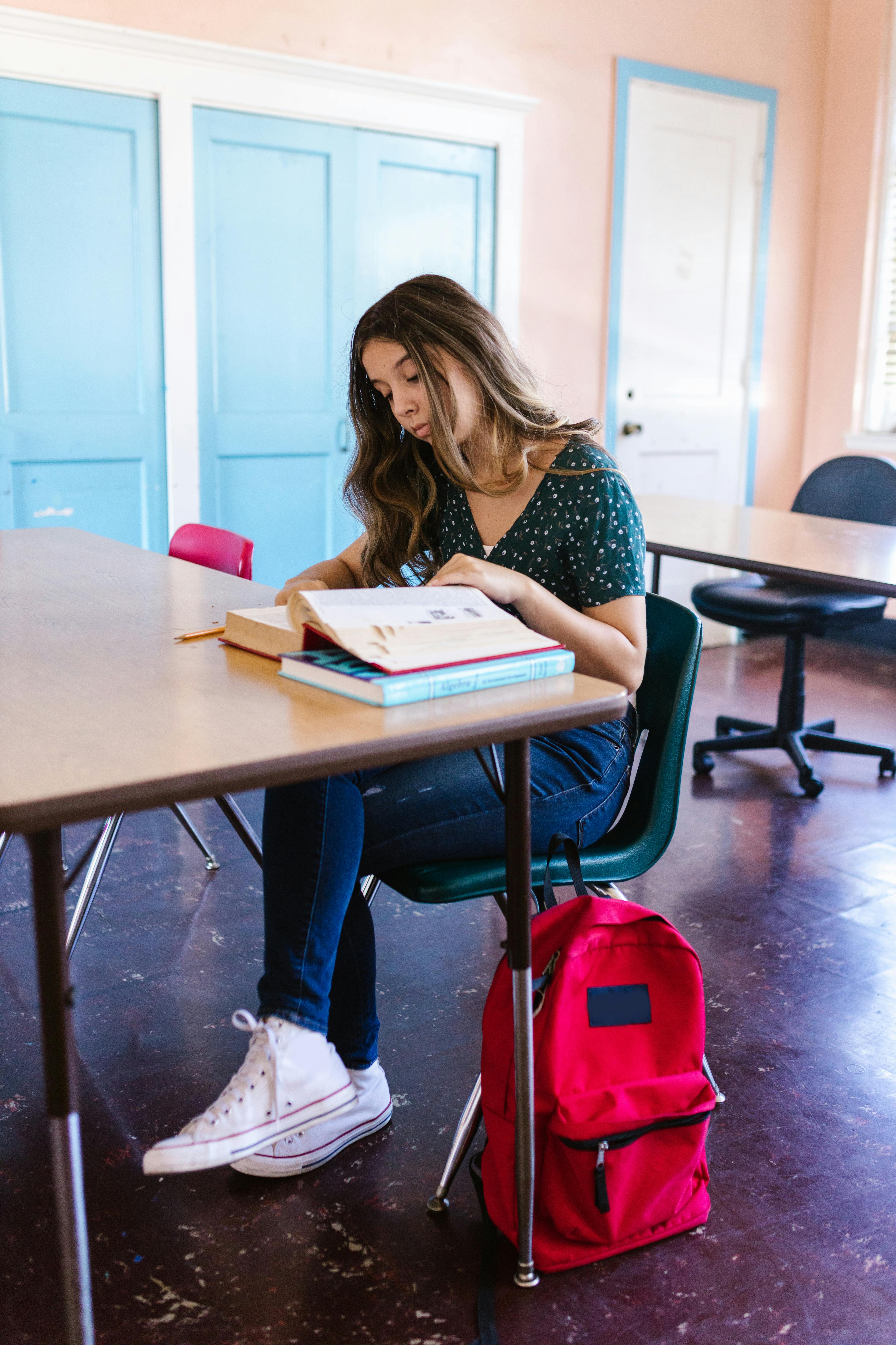 An unhappy girl sitting at a desk with a book in front of her at school | Source: Pexels