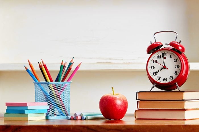 Alarm clock on top of books with school supplies on wooden table. Back to school conceptual image.