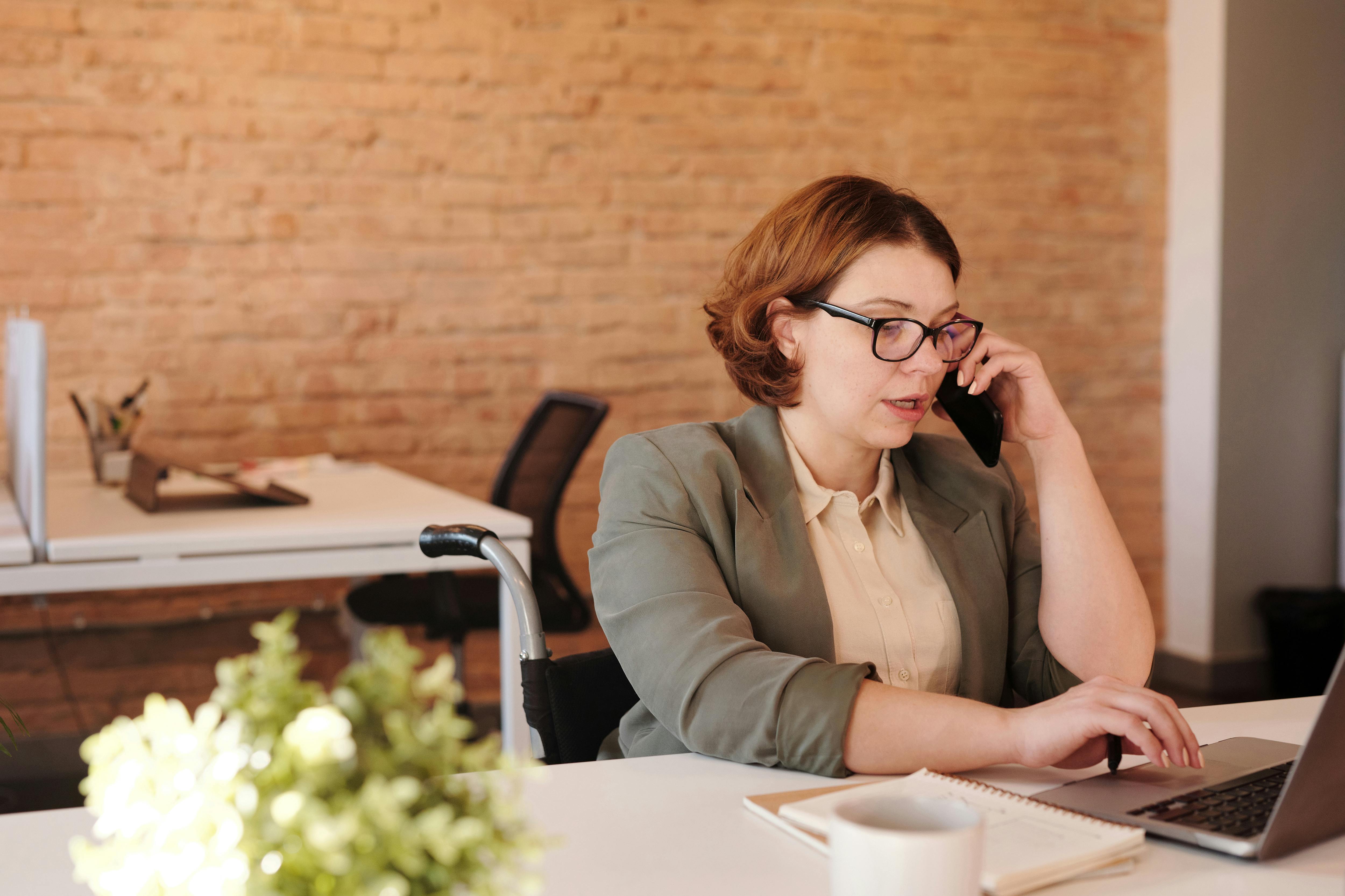 A woman talking on the phone while working on a laptop | Source: Pexels